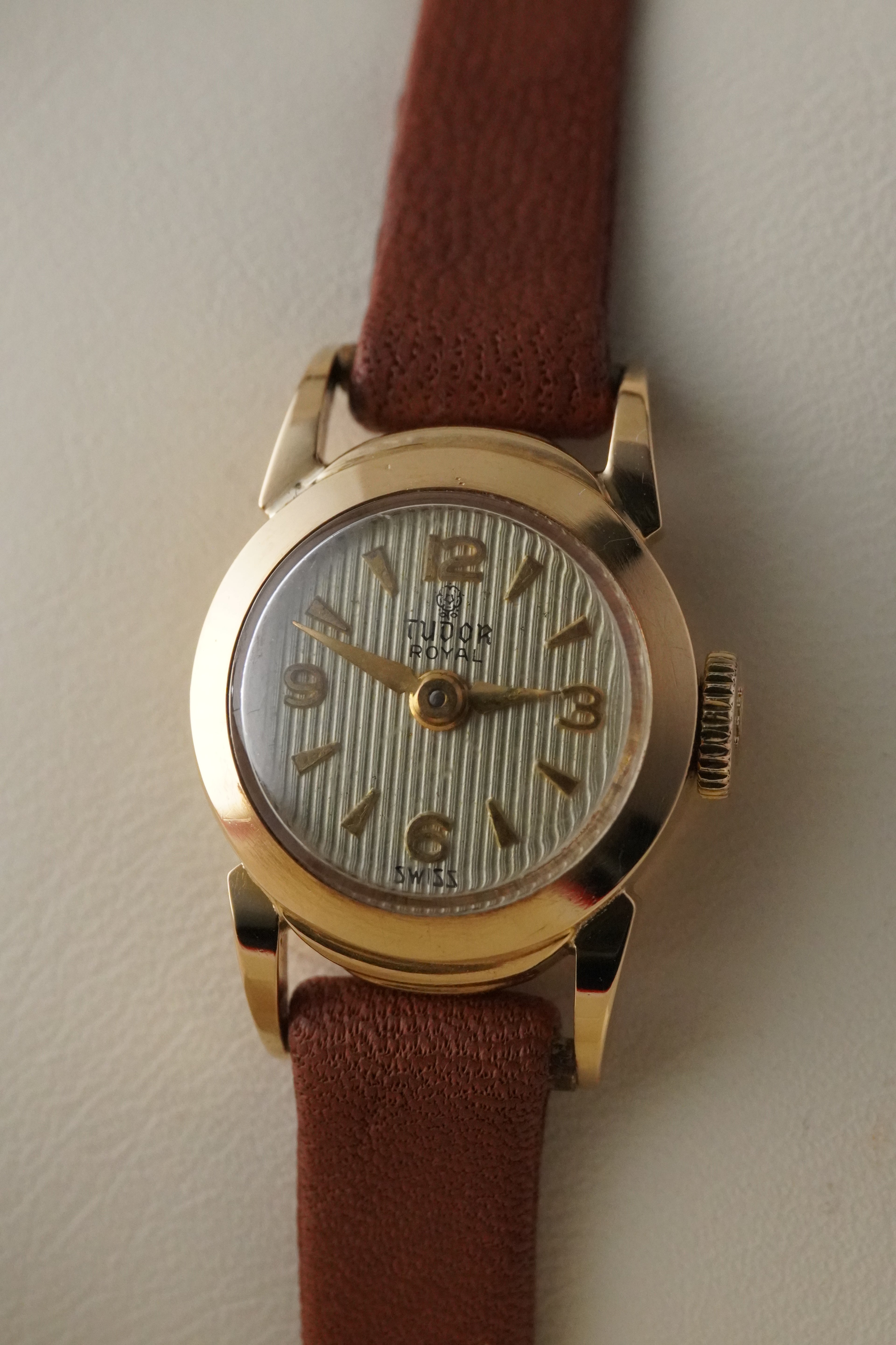 Gold wristwatch with a brown leather strap on a light background