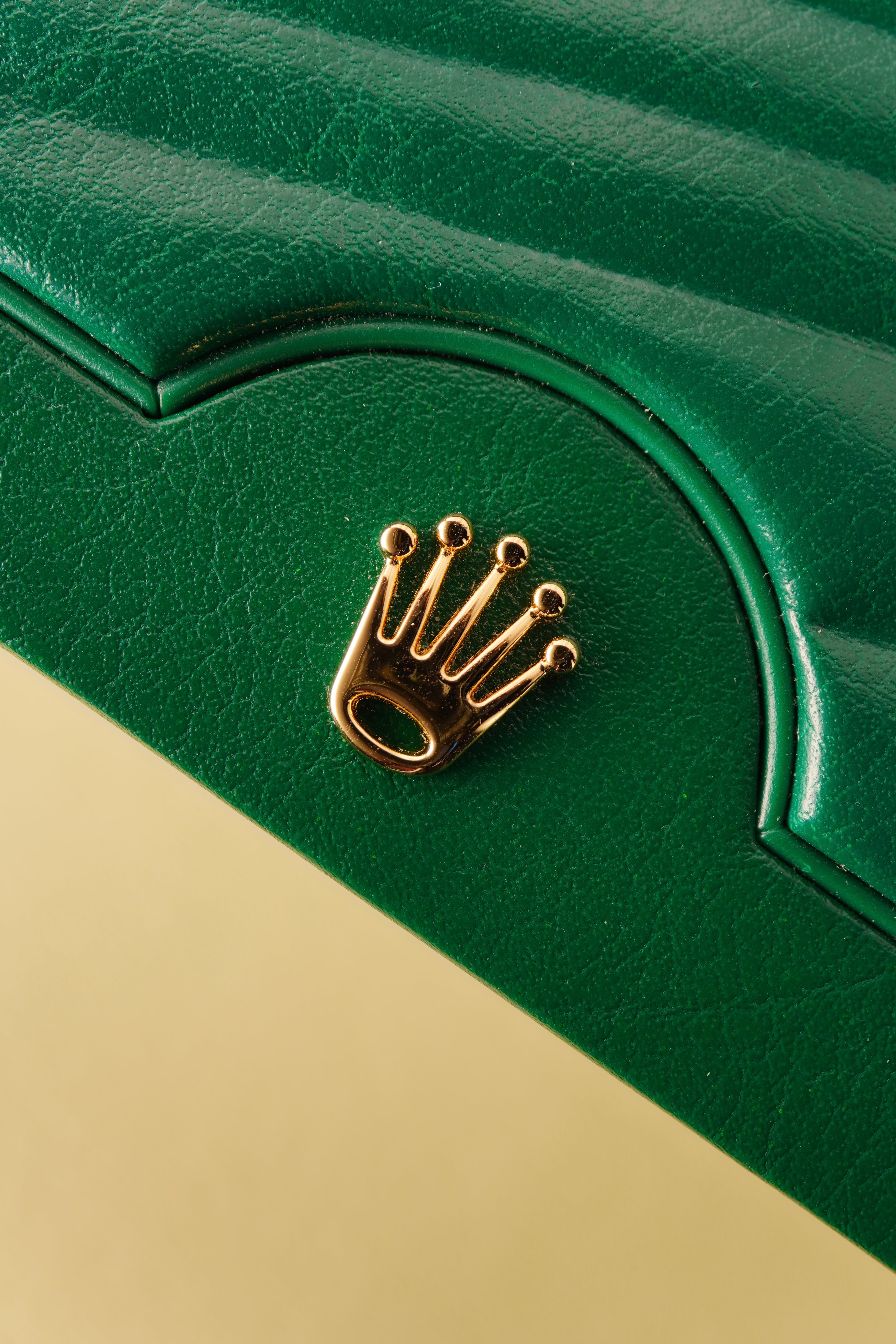 Close-up of a green leather product with a gold crown emblem on a beige background