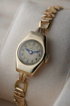 Close-up images of an early 1950s ladies’ Omega wristwatch with a 9ct gold Dennison case, cream dial with Arabic numerals, blued steel hands, inner caseback hallmarkings, and a side profile of the watch.
