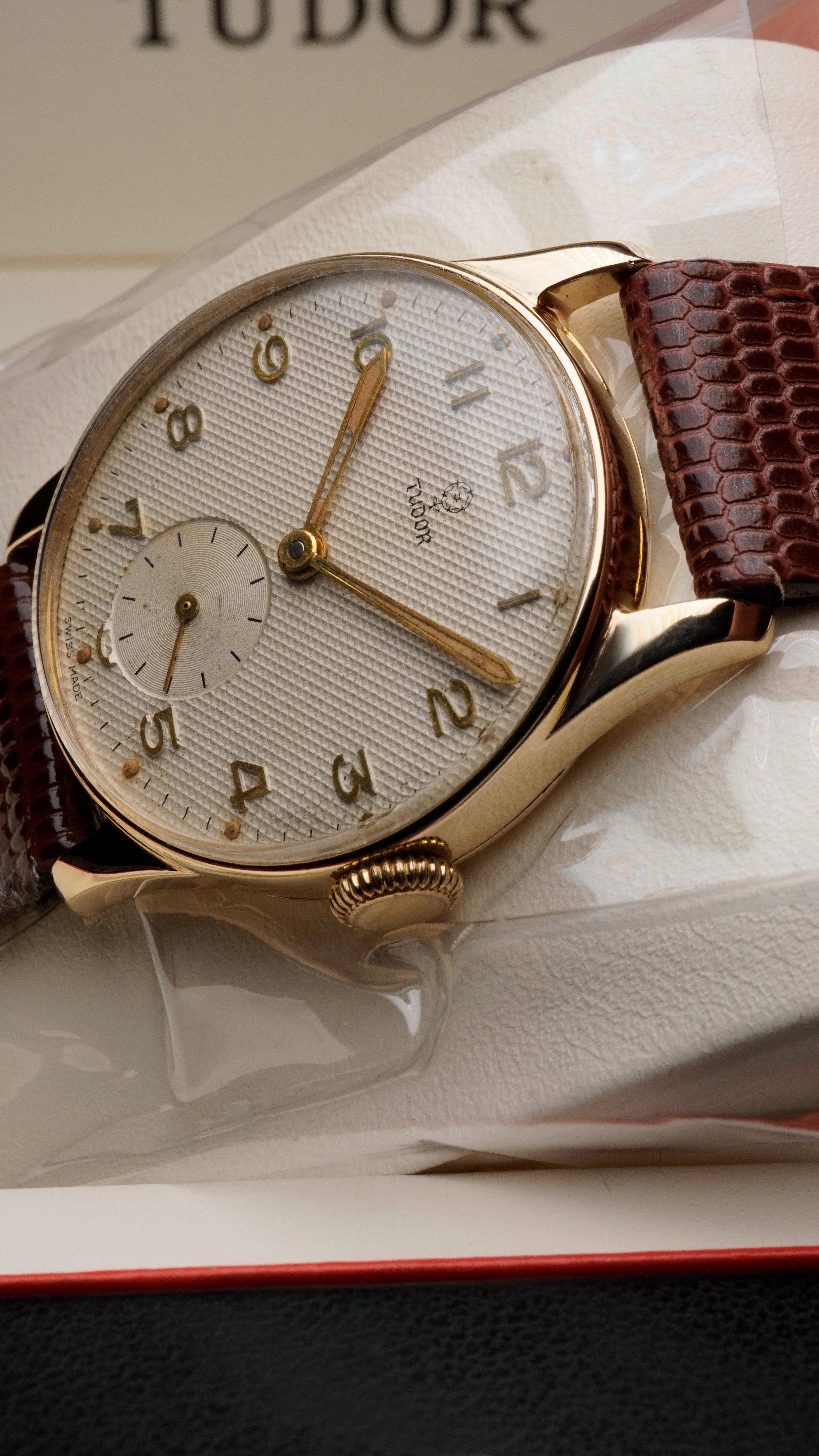 Vintage Tudor wristwatch featuring a textured silver waffle dial with applied Arabic numerals, small seconds sub-dial at 6 o’clock, and a solid 9ct yellow gold case, paired with a brown leather strap.