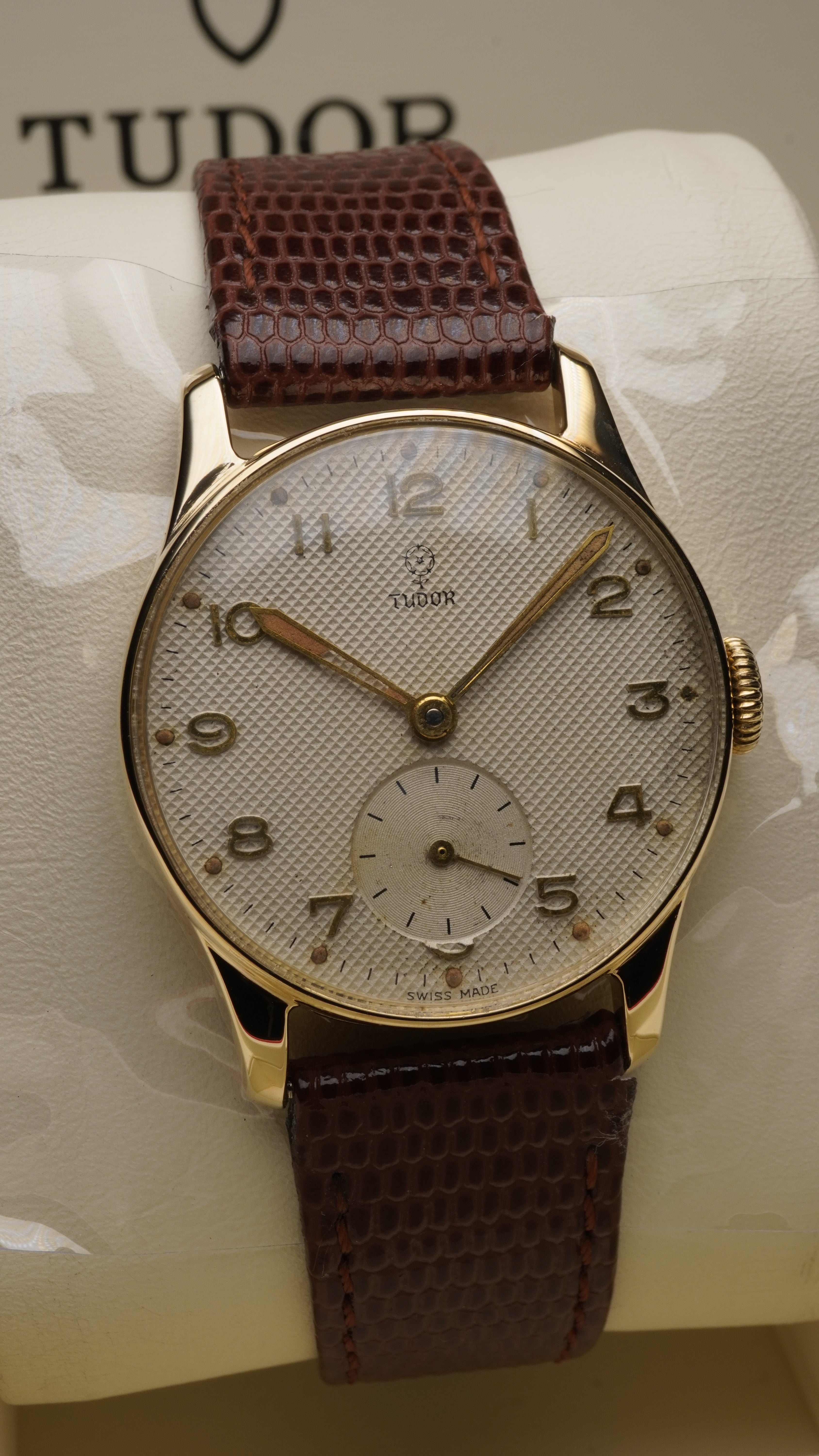 

Vintage Tudor wristwatch featuring a textured silver waffle dial with applied Arabic numerals, small seconds sub-dial at 6 o’clock, and a solid 9ct yellow gold case, paired with a brown leather strap.