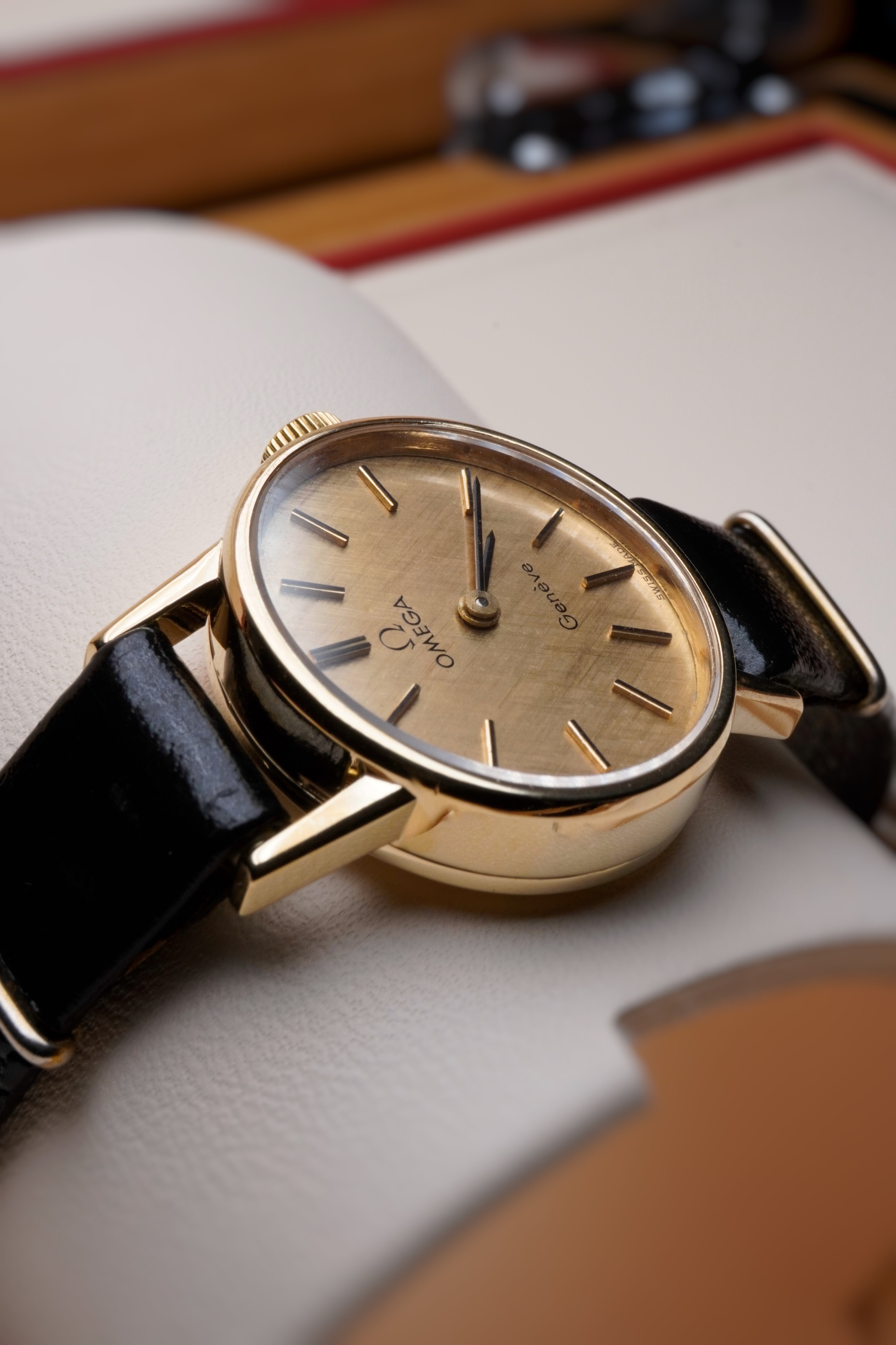 Rare vintage Omega Genève 9ct yellow gold ladies watch with vertical brushed (cadran brossé vertical) dial, gold-tone case, minimalist baton hour markers and black leather strap, Swiss made manual wind dress watch.