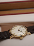 Side view of Vintage Omega ladies dress watch with silver dial, applied baton hour markers, 9ct solid gold case and brown leather strap, displayed in original Omega presentation box.