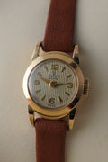 Gold wristwatch with a brown leather strap on a light background