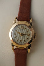 Gold wristwatch with a brown leather strap on a light background