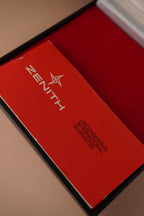 Zenith vintage dress watch with 9ct English-made yellow gold case, silver dial, black leather strap, professionally polished, displayed with original Zenith booklet on red background.