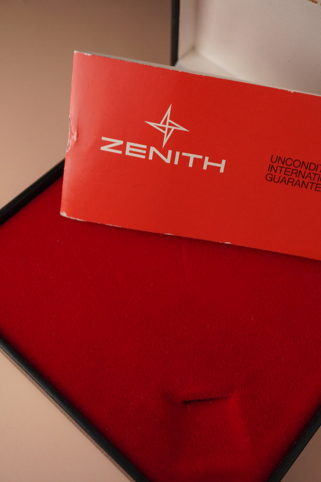 Zenith vintage dress watch with 9ct English-made yellow gold case, silver dial, black leather strap, professionally polished, displayed with original Zenith booklet on red background.