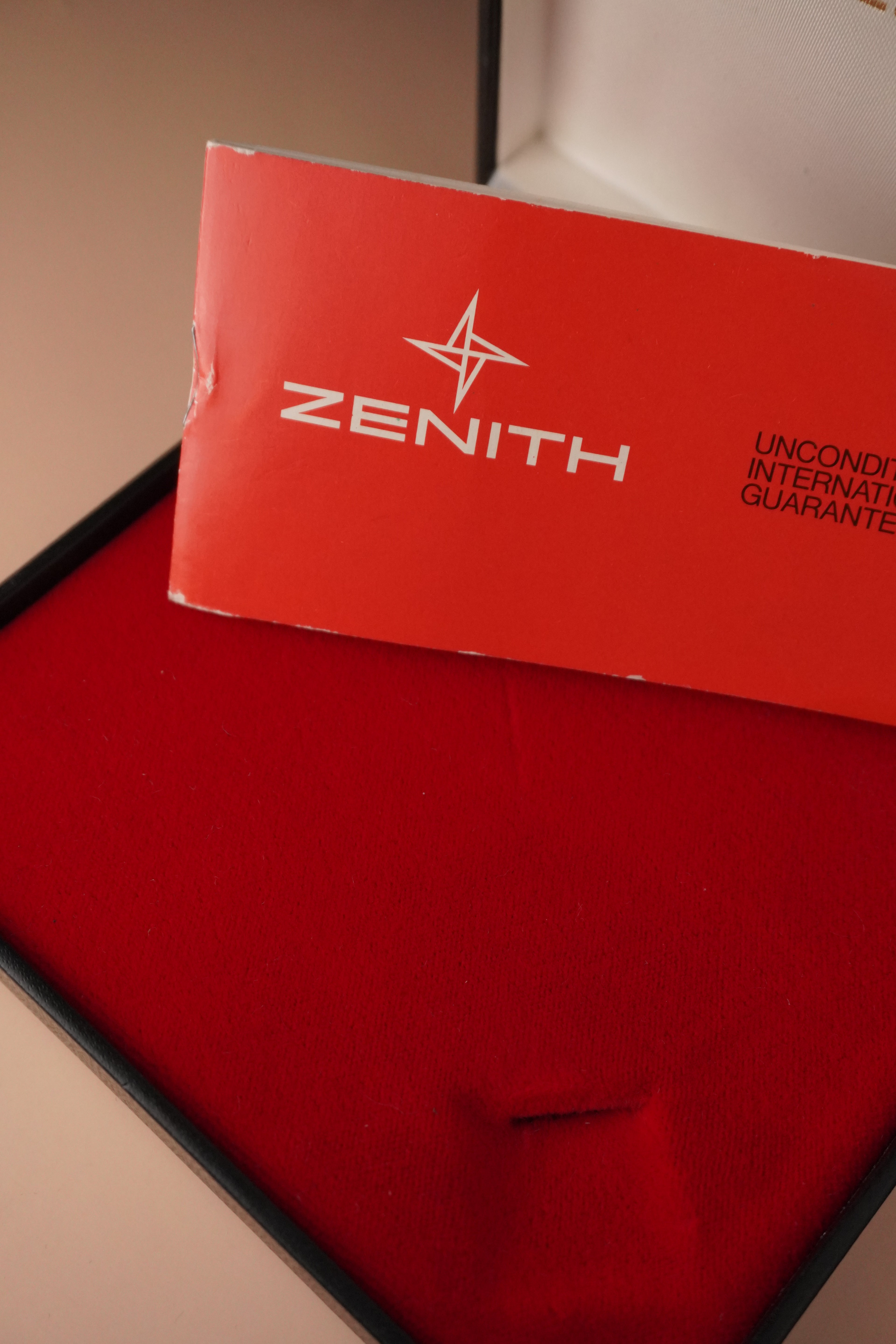 Zenith vintage dress watch with 9ct English-made yellow gold case, silver dial, black leather strap, professionally polished, displayed with original Zenith booklet on red background.