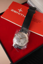 Zenith vintage dress watch with 9ct English-made yellow gold case, silver dial, black leather strap, professionally polished, displayed with original Zenith booklet on red background.