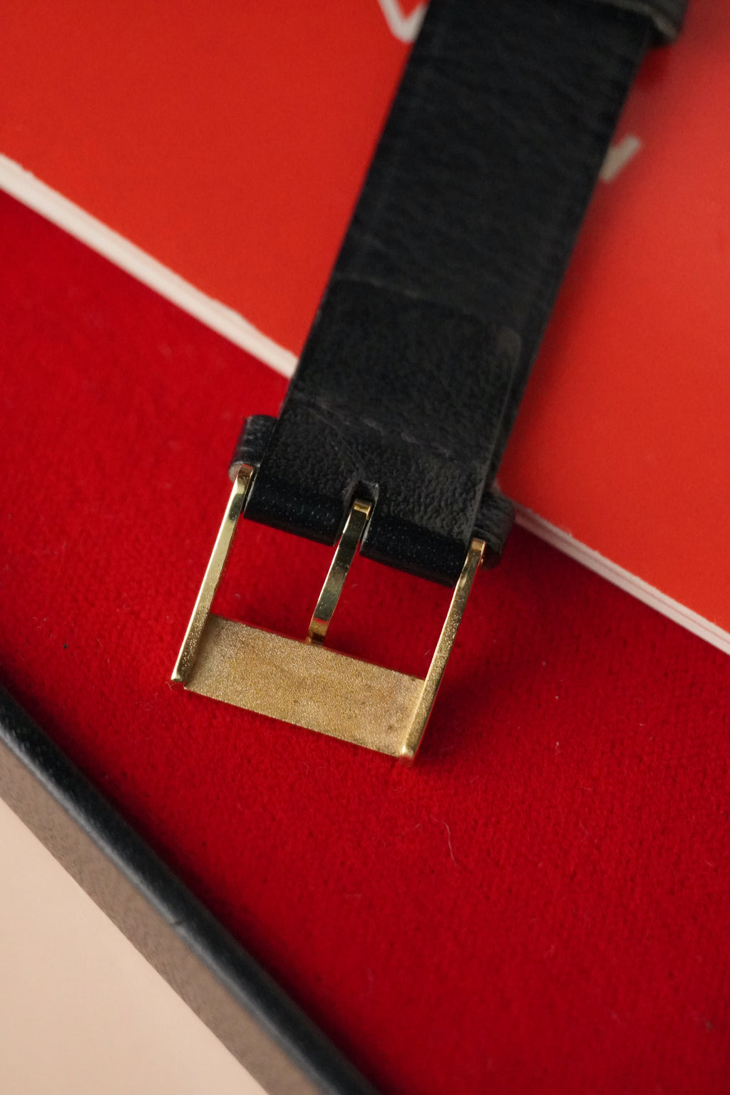 Black watch strap with gold buckle on a red background