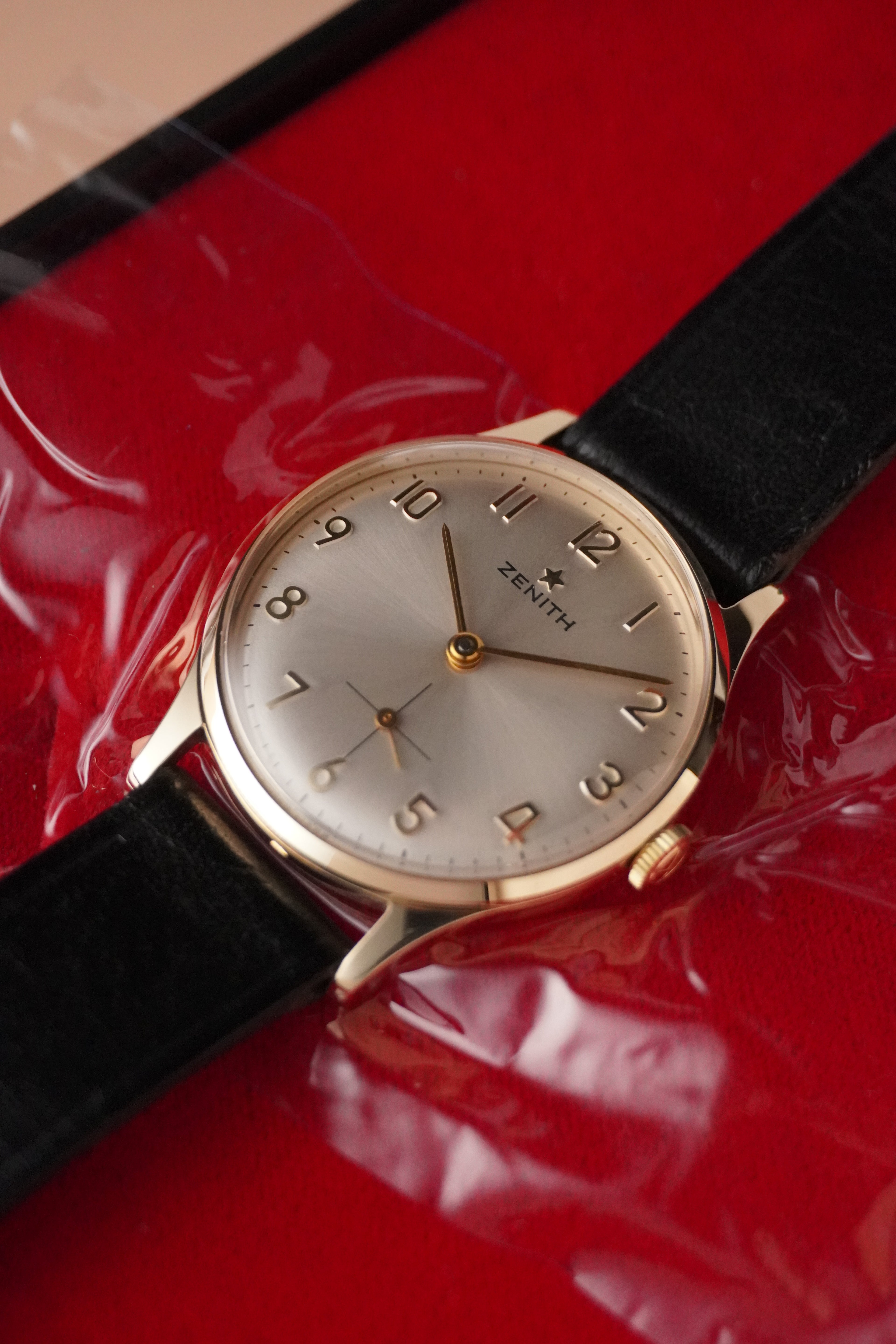 Wristwatch with black strap and gold case on a red surface