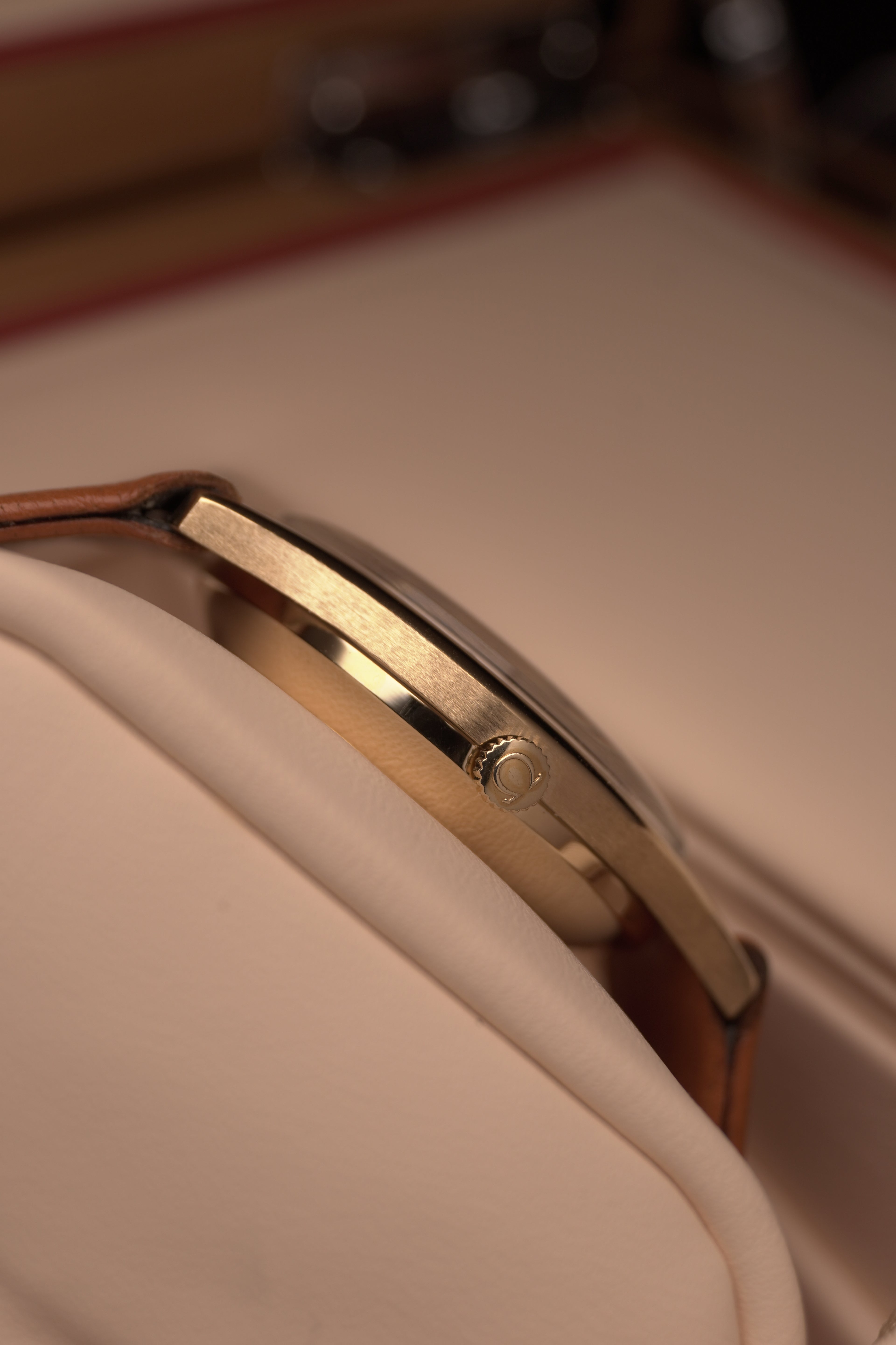 Side profile Angled close-up of a vintage Omega Automatic gents watch in solid yellow gold with a champagne dial, baton hour markers and date window, on a brown leather strap.