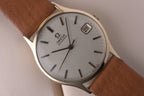 Front view of the vintage Omega Automatic watch showing a brushed silver dial with slim baton markers, central seconds hand and a framed date display at 3 o’clock, fitted to a brown leather strap.