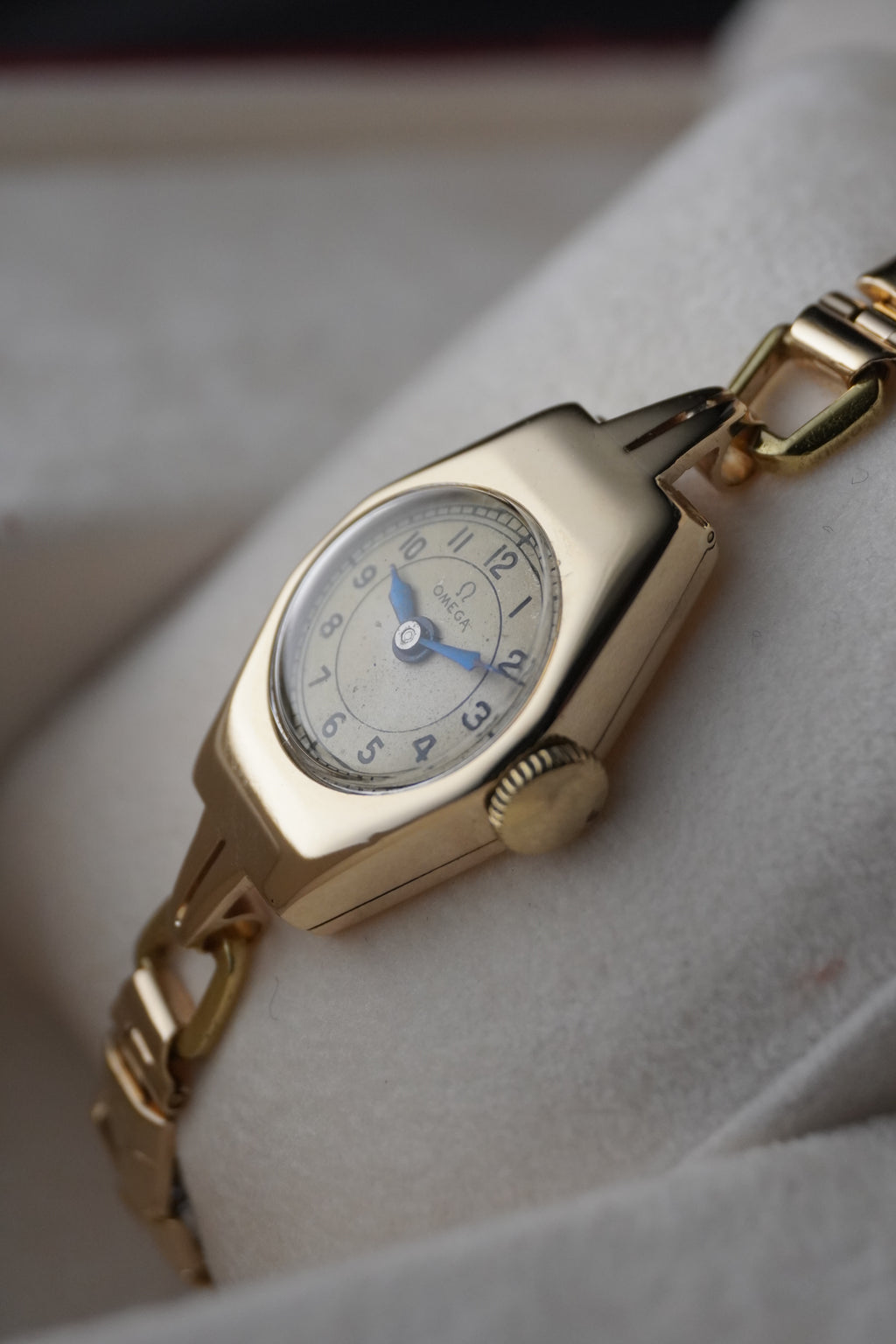 Close-up images of an early 1950s ladies’ Omega wristwatch with a 9ct gold Dennison case, cream dial with Arabic numerals, blued steel hands, inner caseback hallmarkings, and a side profile of the watch.