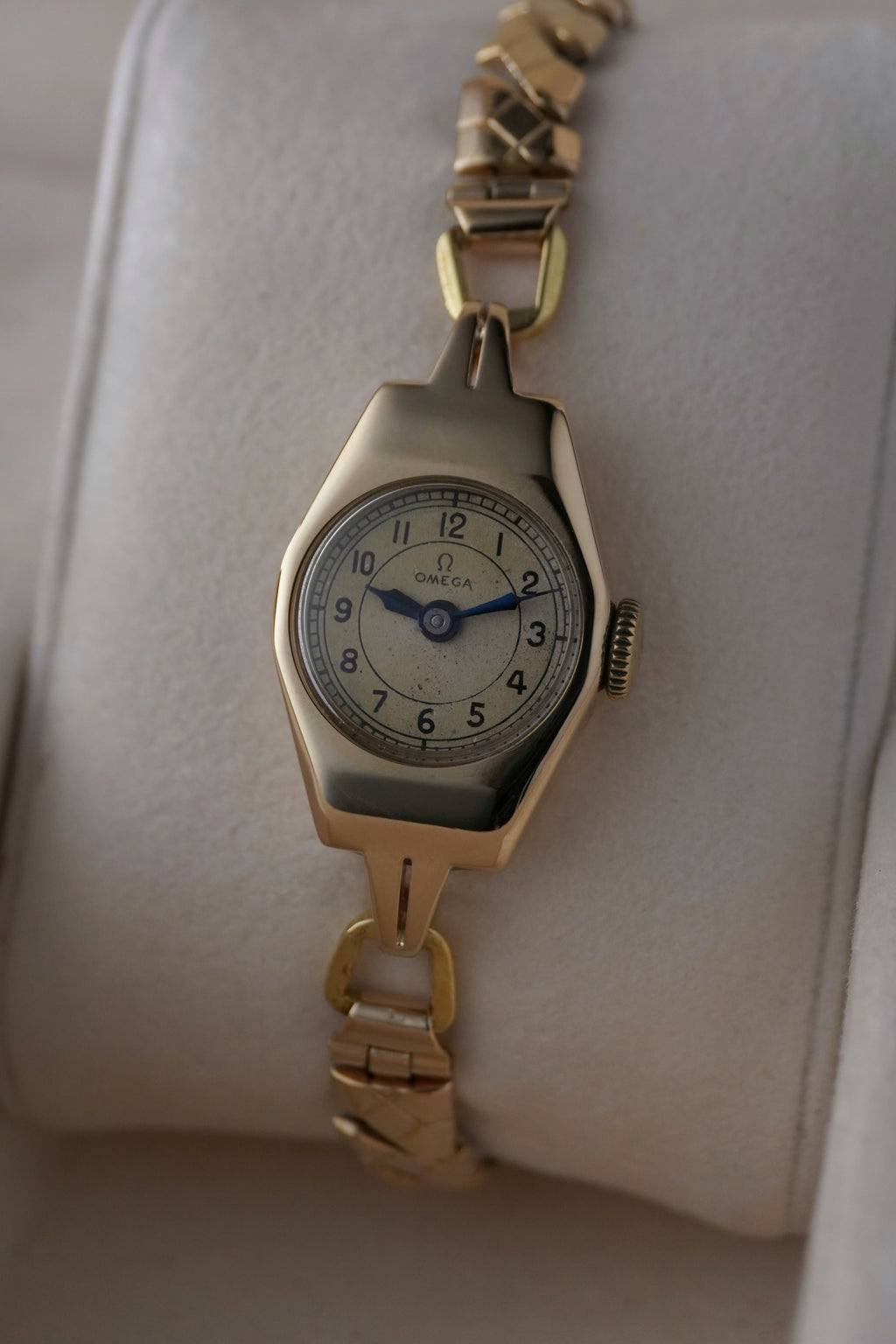 Close-up images of an early 1950s ladies’ Omega wristwatch with a 9ct gold Dennison case, cream dial with Arabic numerals, blued steel hands, inner caseback hallmarkings, and a side profile of the watch.