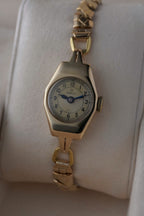 Close-up images of an early 1950s ladies’ Omega wristwatch with a 9ct gold Dennison case, cream dial with Arabic numerals, blued steel hands, inner caseback hallmarkings, and a side profile of the watch.