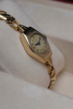 Close-up images of an early 1950s ladies’ Omega wristwatch with a 9ct gold Dennison case, cream dial with Arabic numerals, blued steel hands, inner caseback hallmarkings, and a side profile of the watch.